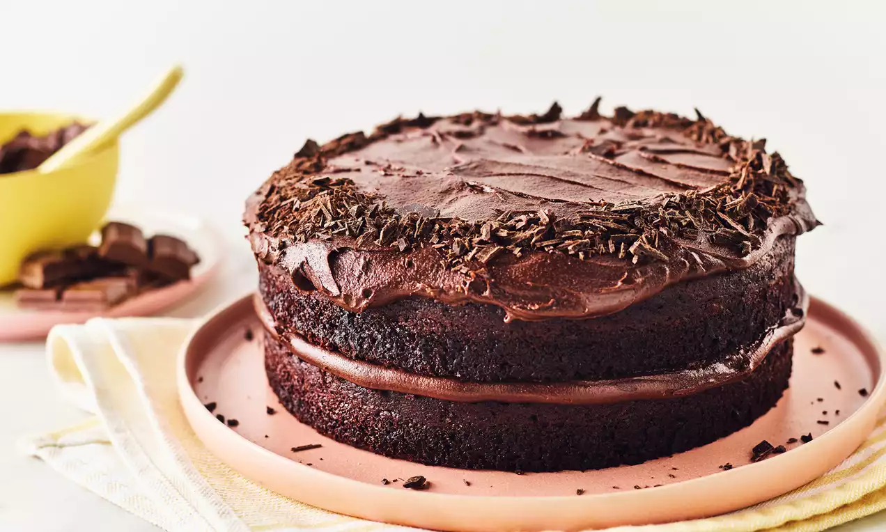 To-lags vegansk sjokoladekake med mørk glasur, dekorert med sjokoladeflak på toppen, servert på rosa fat med lysegule servietter under