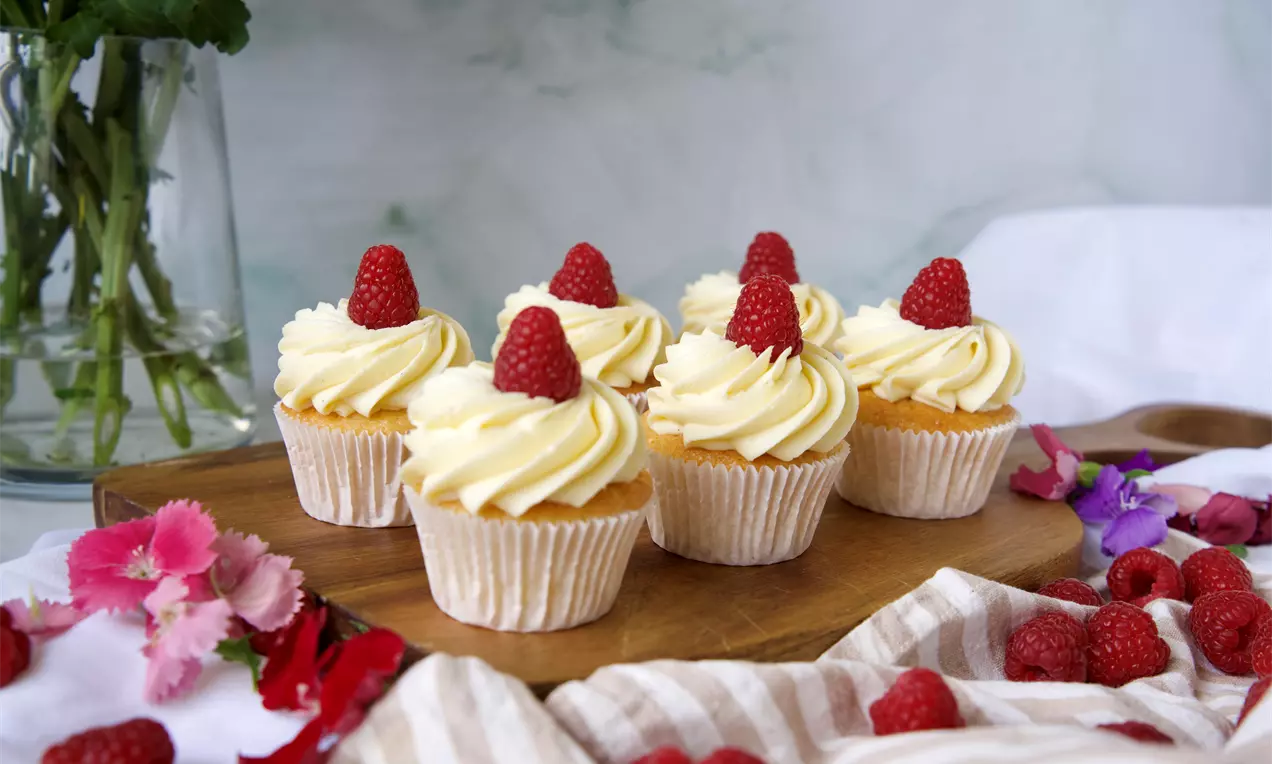 Lyse cupcakes med en swirl av lys frosting toppet med ett bringebær.